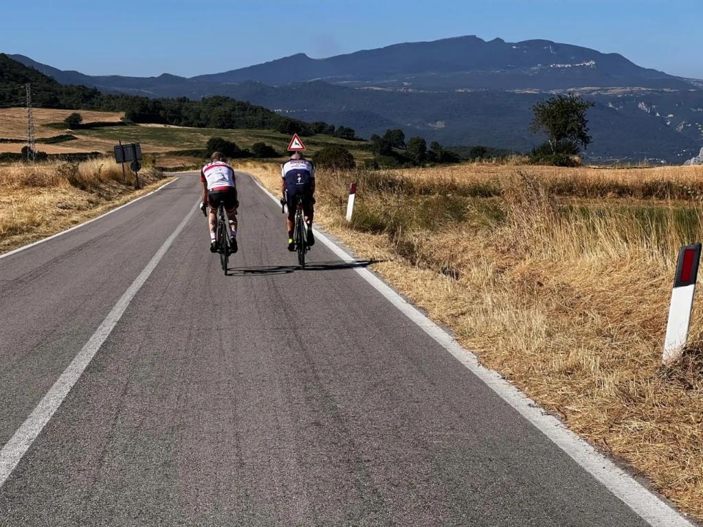 Two cyclists riding on open road with mountain backdrop