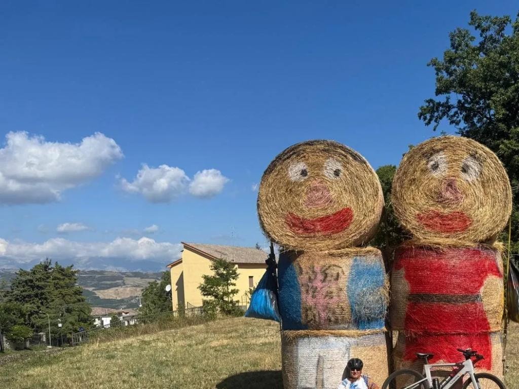 Cyclist posing next to painted hay bale figures in Abruzzo